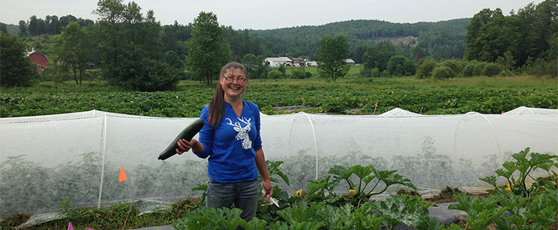 Vermont Gleaning Collective member at Greenhouse holding cucumber